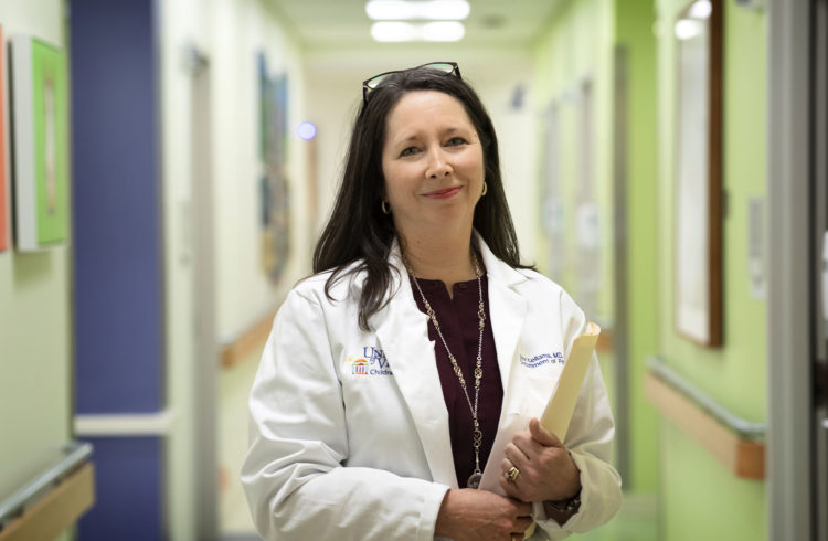 Ann Kellams holds a yellow folder in a hallway outside patient rooms.