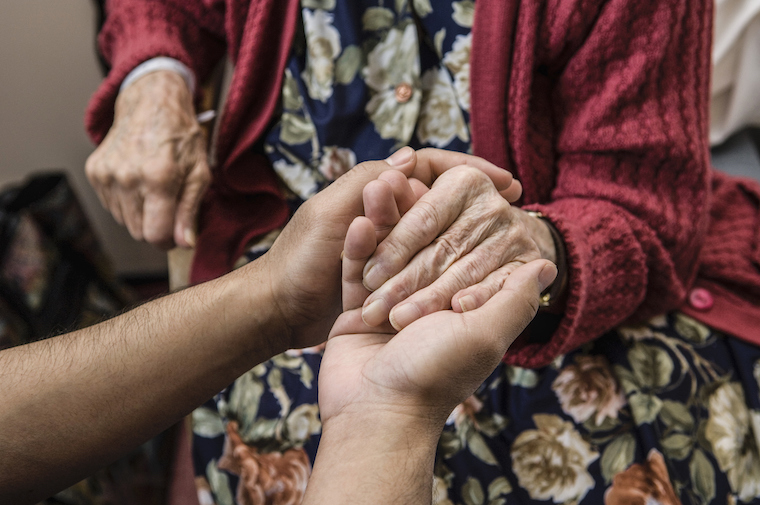 A nurse holds hands with an older woman.