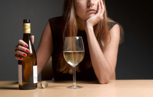 A woman sits forlornly with a big glass of white wine.