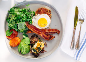 Fried egg, bacon, greens and other keto foods on a plate.
