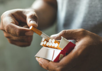 A man pulls a cigarette from a half-empty pack.