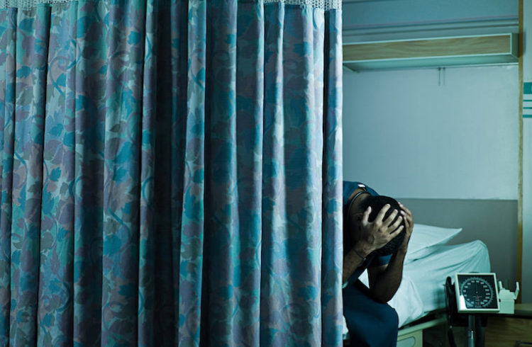 A man clutches his head with anxiety in a hospital room.