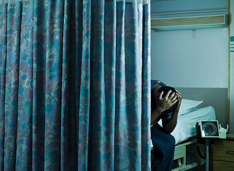 A man clutches his head with anxiety in a hospital room.