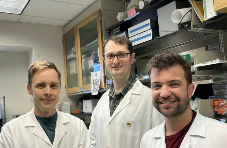 Researchers Stephen Abbott, Daniel Stornetta and George Souza. They are wearing white coats in a lab.