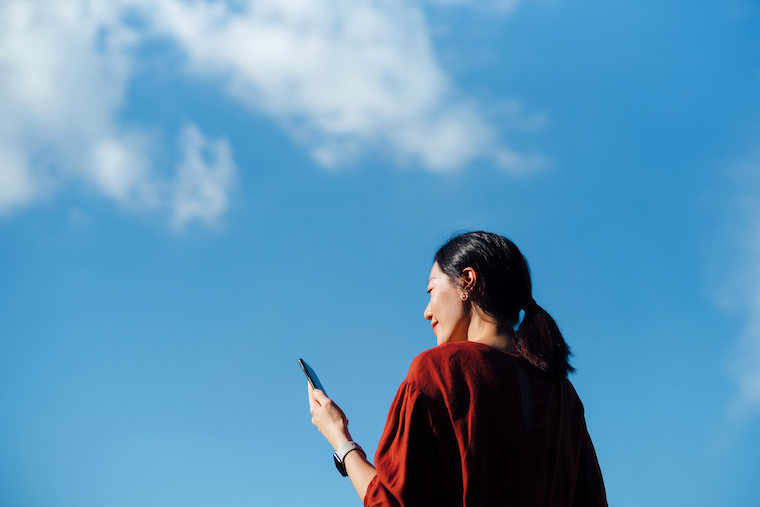 A woman looks at her cell phone in front of a blue sky.