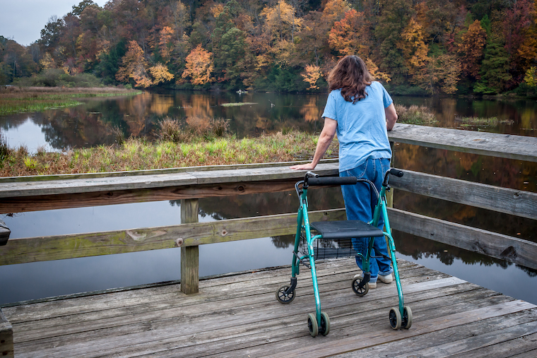 Woman with walker looks out on a lake.