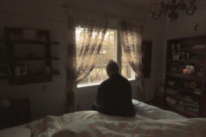 Senior man in dark room looks out window