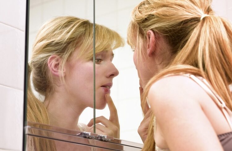 Woman inspecting cold sore in mirror